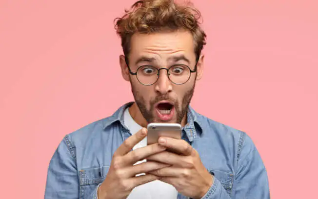 A man photographed while looking at his phone with a expression of surprise.
