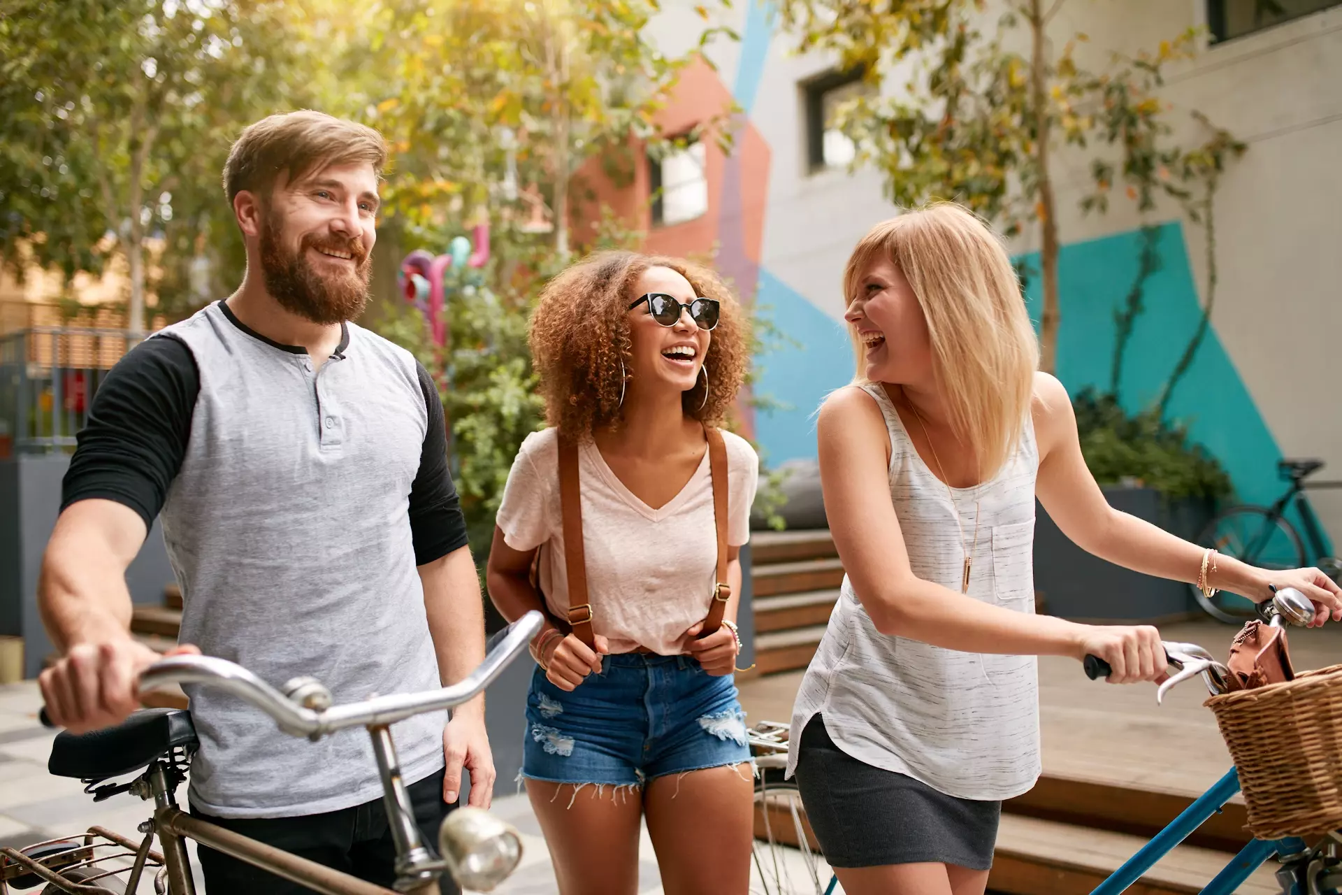 A man and two women share a laugh while taking a walk with bikes on a spring day.